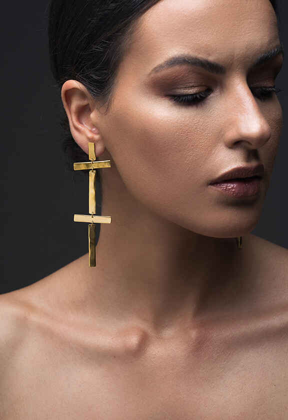 Γυναίκα φοράει χρυσό κρεμαστό σκουλαρίκι Emmanuela